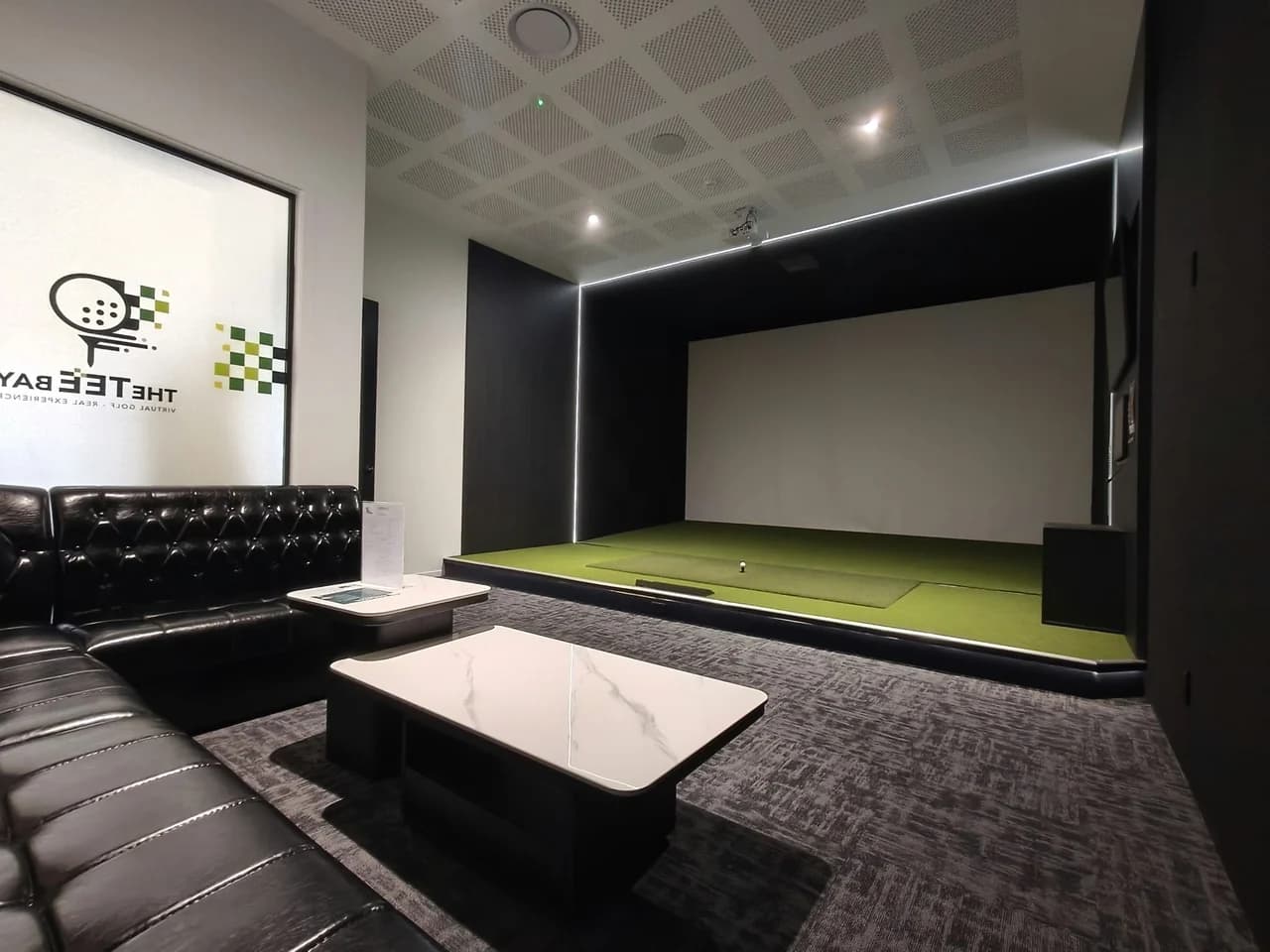 VIP Room 3 at The Tee Bay with a golf simulator, lounge seating and The Tee Bay wall logo